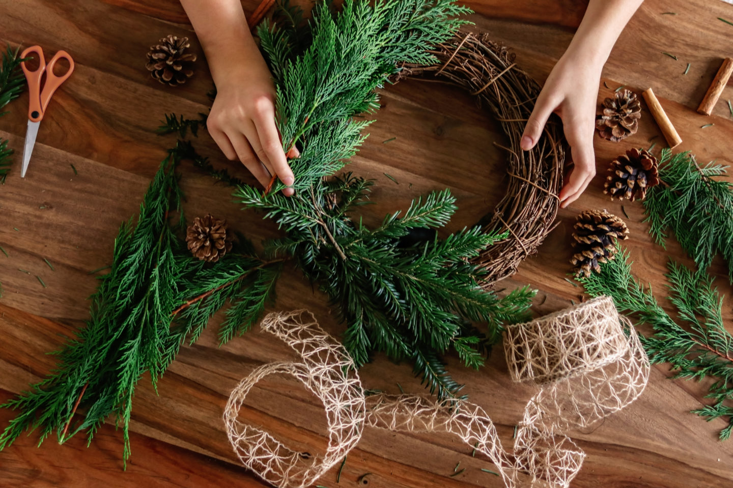 Overhead shot of hands making handmade Christmas wreath with twigs, pine cones, cinnamon sticks, yew and thuja branches and natural string. DIY home decor.