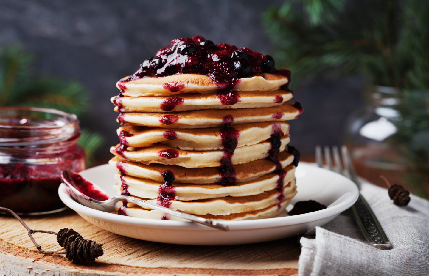 Stack of american pancakes or fritters with strawberry and blueberry jam in white plate on wooden rustic table decorated Christmas tree, delicious dessert for breakfast in winter, vintage style